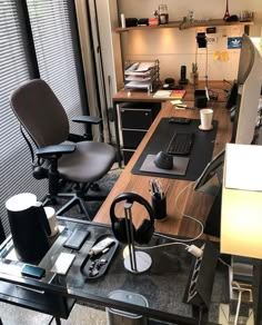 an office desk with a computer and headphones on it in front of a window