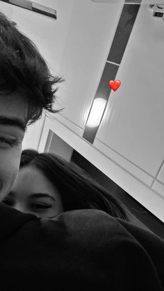 a man and woman cuddle in front of a red heart hanging from the ceiling