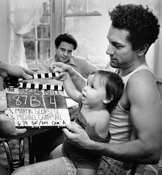 a man holding a baby in front of a movie clapper while three other people watch