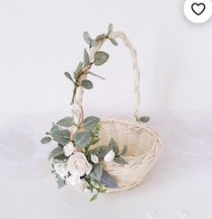 a wicker basket with flowers and greenery in it on a white tablecloth