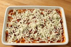 a casserole dish with cheese and sauce in it sitting on a wooden table