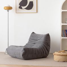 a grey bean bag chair sitting on top of a wooden floor next to a book shelf