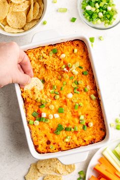 a person dipping tortilla into a casserole dish with vegetables and chips