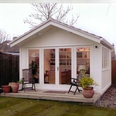 a small white house sitting on top of a grass covered yard next to a wooden fence