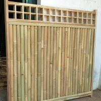 a bamboo fence with lattices on top and bottom part in the foreground, next to a pile of pallets