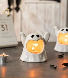 two white ceramic ghost tea light holders with candles in front of them on a table