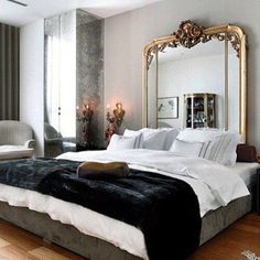 a large bed sitting in a bedroom next to a tall mirror on top of a wooden floor