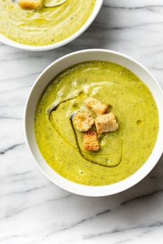 two bowls filled with soup and croutons on top of a marble countertop