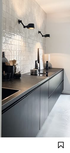 a modern kitchen with stainless steel counter tops and black cabinets, along with white tiles on the wall