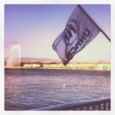 a flag is flying over the water with buildings in the background