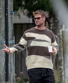 a man in a striped sweater holding out his hand while standing next to a pole