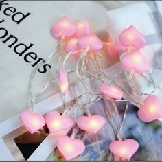 pink heart shaped string lights are on the table next to an open book and magazine