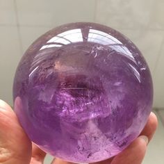 a person holding a purple crystal ball in their hand with white tiles on the wall behind it