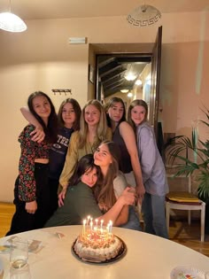 a group of young women standing around a birthday cake with lit candles on top of it