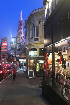 people are walking down the sidewalk in front of shops and buildings at night with lights on