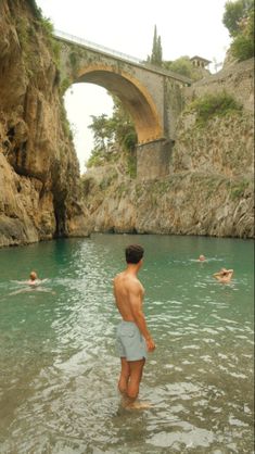 a man standing in the middle of a body of water next to a stone bridge