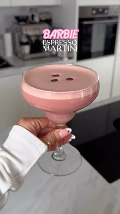 a woman holding up a pink drink with a smiley face on the side and text barbie espresso martini