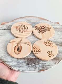 four wooden coasters with bees and honeycombs on them, one being held by a hand