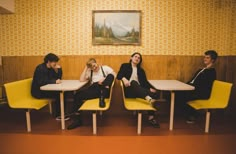 four people sitting at a table in a room with yellow chairs and a painting on the wall