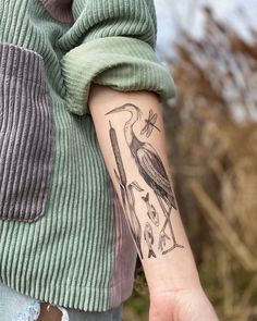 a person with a bird tattoo on their arm holding something in one hand and two birds on the other