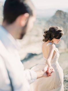 a woman in a white dress standing next to a man on top of a mountain