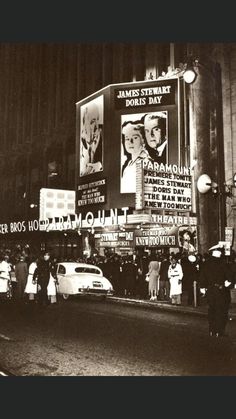 an old black and white photo of people standing in front of a movie theater at night