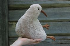 a hand holding a stuffed bird in front of a wooden wall with peeling paint on it