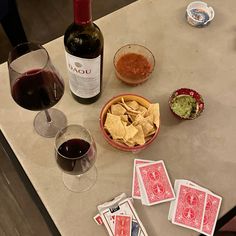 wine, chips and salsa sit on a table next to two glasses of red wine