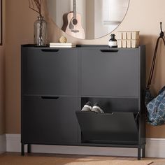 a black cabinet with two drawers and a guitar hanging on the wall next to it