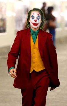 a man in a red suit and yellow shirt is walking down the street wearing a clown mask