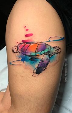 a watercolor style turtle tattoo on the right thigh, with colorful paint splatters all over it