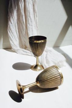 two golden goblets sitting next to each other on a white tableclothed surface