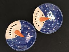 two blue and white plates with a snowman face painted on one side and an orange nose on the other