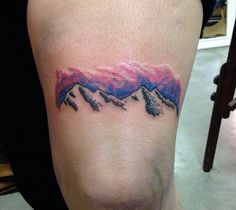 a woman with a tattoo on her arm that has mountains in the sky and pink clouds