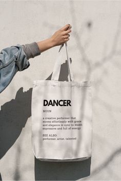 a person holding a white bag that says dancer on it, against a concrete wall