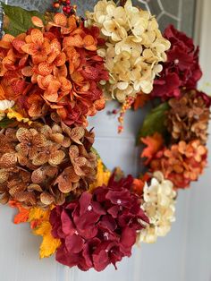 the wreath is decorated with flowers and leaves on it's front door, as well as an orange hydrangea