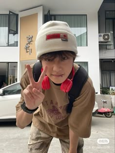 a young boy making the peace sign in front of a building with cars behind him