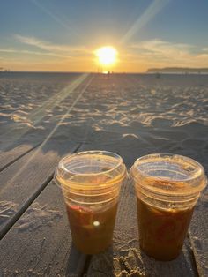 two plastic cups filled with liquid sitting on top of a wooden table next to the ocean