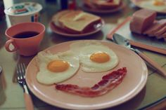 two fried eggs and bacon on a pink plate with coffee in front of them at a breakfast table