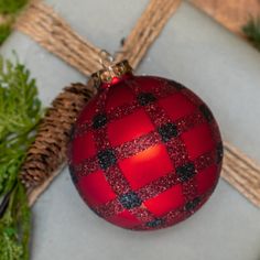 a red ornament sitting on top of a table next to some pine branches