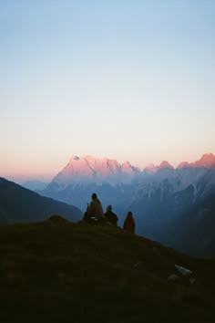 three people sitting on top of a hill with mountains in the background