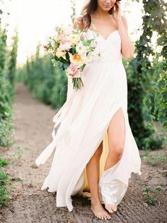 a woman wearing a white dress and holding a bouquet in her hand walking down a dirt path