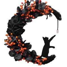 a wreath with orange berries and black cat silhouettes on the front, against a white background