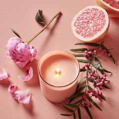 a candle and some flowers on a pink surface with grapefruits around it