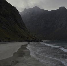 an ocean with mountains in the background and water on the beach at night, under a cloudy sky