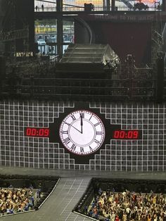 a large clock on the side of a building with people sitting in seats around it