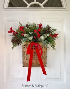 a basket filled with red berries and greenery hanging on a white front door decorated for christmas