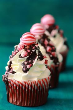 three cupcakes with white frosting and candy canes sitting on top of each other