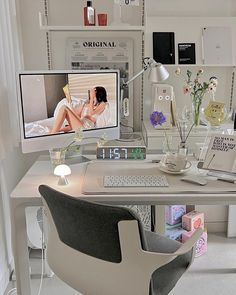 a desk with a computer monitor, keyboard and mouse next to a vase filled with flowers