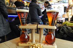 two glasses of beer sitting on top of a wooden table next to some corn kernels